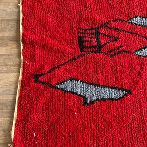 Peut inclure: Un tapis &eacute;pais &agrave; poils longs pr&eacute;sentant un fond rouge vif avec un grand motif graphique abstrait. Le design se compose de contours noirs audacieux entourant des formes remplies d'une couleur gris clair, cr&eacute;ant un aspect textur&eacute; et nou&eacute; &agrave; la main.
