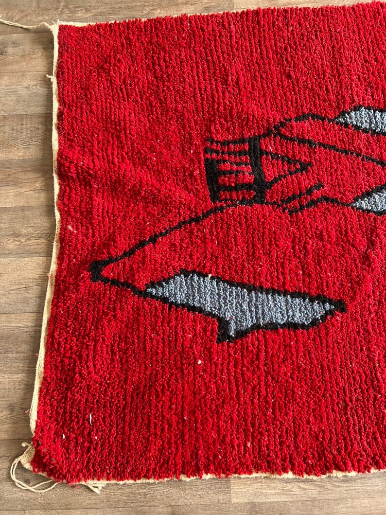 Peut inclure: Un tapis &eacute;pais &agrave; poils longs pr&eacute;sentant un fond rouge vif avec un grand motif graphique abstrait. Le design se compose de contours noirs audacieux entourant des formes remplies d'une couleur gris clair, cr&eacute;ant un aspect textur&eacute; et nou&eacute; &agrave; la main.
