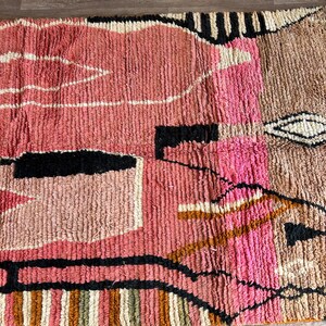 May include: A colorful, abstract rug with geometric shapes in shades of pink, brown, black, and white. The rug has a hand-woven texture and a modern design.