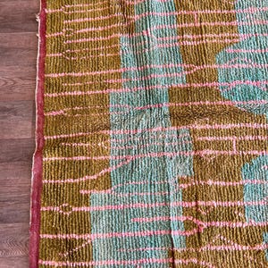 May include: A rectangular rug with a textured, woven design. The rug features a colour block pattern with sections of olive green, light blue, and pink stripes. The edges are trimmed with a red border.