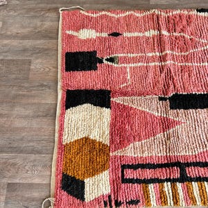May include: A pink, black, white, and brown geometric rug with a textured, woven design. The rug has a fringe border.