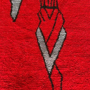 Peut inclure: Un tapis rouge vif pr&eacute;sentant un motif graphique abstrait et stylis&eacute; en noir et gris clair. Le design se compose de lignes angulaires nettes et de formes g&eacute;om&eacute;triques cr&eacute;ant un effet visuel audacieux et contrast&eacute; sur la surface textur&eacute;e.