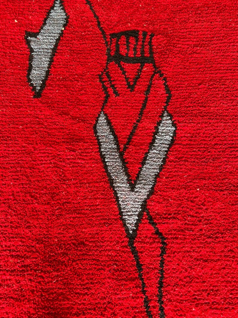 Peut inclure: Un tapis rouge vif pr&eacute;sentant un motif graphique abstrait et stylis&eacute; en noir et gris clair. Le design se compose de lignes angulaires nettes et de formes g&eacute;om&eacute;triques cr&eacute;ant un effet visuel audacieux et contrast&eacute; sur la surface textur&eacute;e.