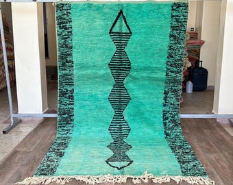 May include: A large, rectangular rug with a turquoise field and black geometric designs. The rug features a central vertical pattern of diamond shapes and a black border on each side. The rug has a fringe along the bottom edge.