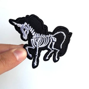 May include: Black iron-on patch with a white embroidered skeleton unicorn design.