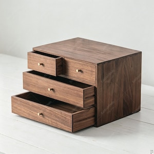 May include: A dark brown wooden desktop organizer featuring four drawers of varying sizes. The unit is constructed from solid wood with visible grain patterns and is equipped with small, round, metallic gold-toned knobs on each drawer front.