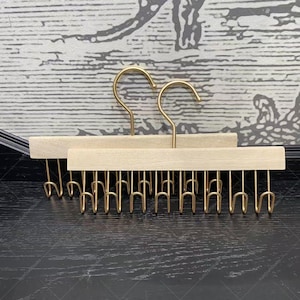 Puede incluir: Dos perchas de madera para bufandas con ganchos dorados. Cada percha tiene un acabado de madera natural y un gancho dorado curvado para colgar. La parte inferior de cada percha tiene múltiples ganchos pequeños para bufandas o accesorios.