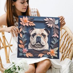 May include: A woman holds a framed paper art piece featuring a bulldog with a floral design. The bulldog is brown and white with a black nose and eyes. The flowers are pink, orange, and yellow. The frame is dark blue.