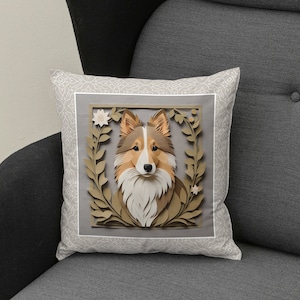Puede incluir: Una almohada decorativa con un fondo beige que presenta un diseño de papel recortado de un perro Shetland con pelaje marrón y blanco. El perro está rodeado de una corona floral con hojas marrones y flores blancas.
