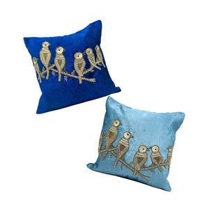 May include: Two decorative throw pillows with embroidered birds on a branch. The pillow on the left is a deep blue velvet with gold birds. The pillow on the right is a light blue velvet with gold birds.