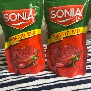 May include: Two red and green Sonia Tomato Mix pouches. The pouches have a red background with a tomato illustration and the words "Tomato Mix" in yellow. The brand name "SONIA" is in white letters on a red and white shield.