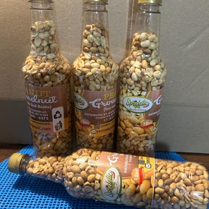 May include: Three clear plastic bottles filled with roasted peanuts. The bottles are labeled "Spedelic Grow" and "Peanut Indncel". The bottles are 12oz and have a gold lid.