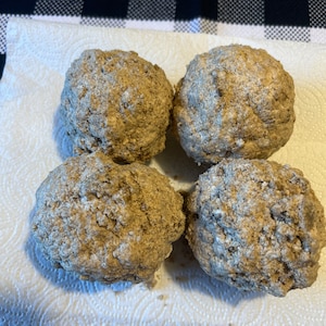 May include: Four round, brown, baked goods on a white paper towel. The goods have a rough, crumbly texture.