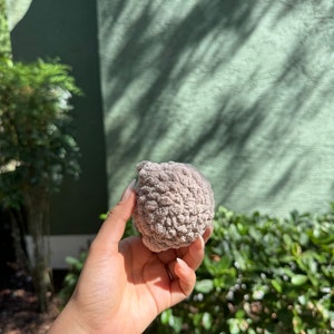 May include: A close-up of a gray, textured, round crocheted object. The object is being held in a person's hand.