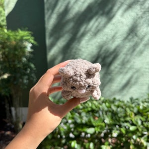 May include: A small, gray, plush toy shaped like a bear with a pink nose and black eyes. The toy is being held in a person's hand.