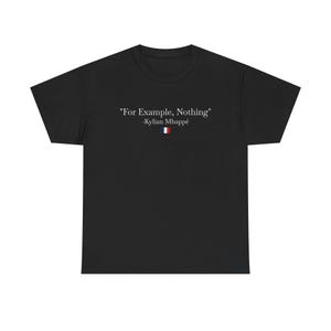 以下が含まれることがあります： 胸の中央に「For Example, Nothing」という白いテキストと、その下に「-Kylian Mbappé」、さらに青、白、赤の縦縞が入った小さな水平の三色旗のアイコンがプリントされた、黒い半袖のTシャツです。