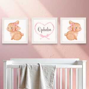 May include: Three framed prints with a watercolor illustration of a brown bunny with a pink bow. The middle print has a pink ribbon heart with the name "Ophelia" written inside.