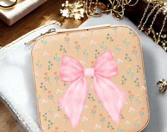 May include: A small, square, beige jewelry box with a zipper closure. The box has a pink bow and a floral pattern.