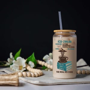 May include: A clear glass tumbler with a bamboo lid and a clear straw, filled with a creamy beverage. The tumbler features the text "ICD-Z99.88" and "Caffeine Dependence - Essential for Coders" with medical symbols and book graphics. The text "The Real ICD Code" is also visible.