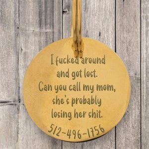 Round gold engraved pet ID tag with funny message that reads “I fcked around and got lost. Can you call my mom, she’s probably losing her sht.” with phone number at bottom. Sturdy metal dog tag with custom etching, durable high-quality plating, and easy-to-attach loop. Perfect for dogs with personality, this humorous pet accessory ensures safety with clear contact info while adding a playful touch.