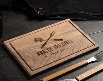 May include: A wooden cutting board with the text "King of the Grill" and a personalized name, "Jason Smith". The board features a graphic of a spatula and a grill fork.