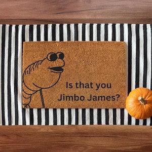May include: A rectangular doormat with the text "Is that you Jimbo James?" and a cartoon character illustration. The mat is brown, with a black and white striped runner underneath and a small orange pumpkin.