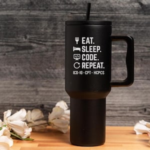 May include: Black insulated tumbler with a handle and a black lid. The tumbler has the words "EAT. SLEEP. CODE. REPEAT." in white, along with "ICD-10 - CPT - HCPCS." A black straw is inserted into the lid.