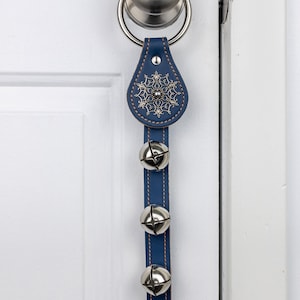 Könnte beinhalten: Ein blauer Türklopfer aus Leder mit einem silbernen Schneeflockenmuster und drei silbernen Glocken, die daran hängen.