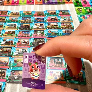 May include: A rectangular trading card featuring a purple background and a cartoon hamster character named Apple. The card displays various icons, the number 359, and the text Apple 9/24. It is surrounded by numerous other similar character cards.
