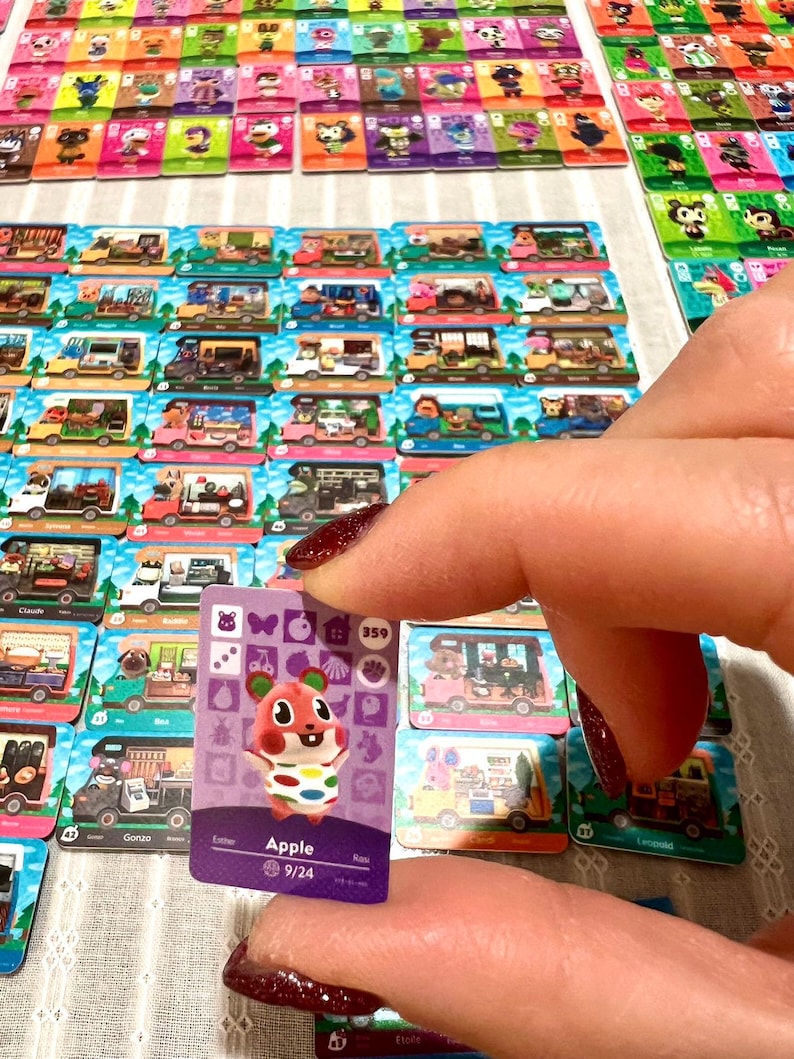 May include: A rectangular trading card featuring a purple background and a cartoon hamster character named Apple. The card displays various icons, the number 359, and the text Apple 9/24. It is surrounded by numerous other similar character cards.