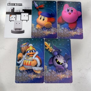 Op de afbeelding: Een verzameling van vijf rechthoekige spelkaarten met karakterillustraties. E&eacute;n witte kaart toont de tekst BOX BOY! met een afbeelding. Vier blauwe kaarten bevatten de personages Kirby, Bandana Waddle Dee, King Dedede en Meta Knight.