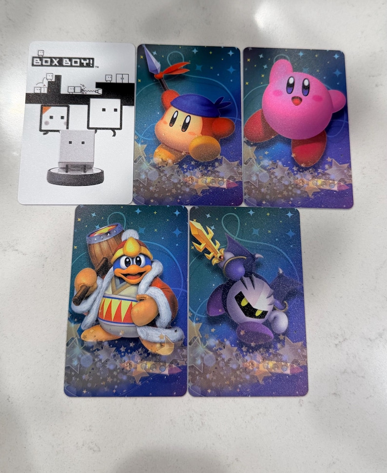 Op de afbeelding: Een verzameling van vijf rechthoekige spelkaarten met karakterillustraties. E&eacute;n witte kaart toont de tekst BOX BOY! met een afbeelding. Vier blauwe kaarten bevatten de personages Kirby, Bandana Waddle Dee, King Dedede en Meta Knight.