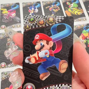 May include: A trading card featuring Mario from the Mario Kart series. Mario is shown in his red hat and blue overalls, holding a kart. The card has a black background with a checkered pattern and various icons.