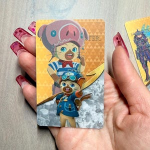 May include: A rectangular card featuring two cartoon characters in a colorful design. The top character wears a pig-themed hat, while the bottom character wears a blue outfit and goggles. The word "TER" is visible on the card.