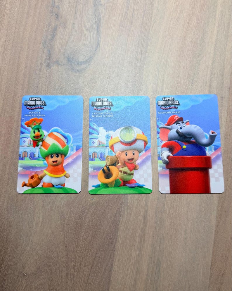 Puede incluir: Tres tarjetas coleccionables de Super Mario Bros. Wonder. Las tarjetas presentan a Poplin & Prince Florian, Captain Toad & Talking Flower y Elephant Mario. Cada tarjeta tiene un fondo azul con ilustraciones de personajes.