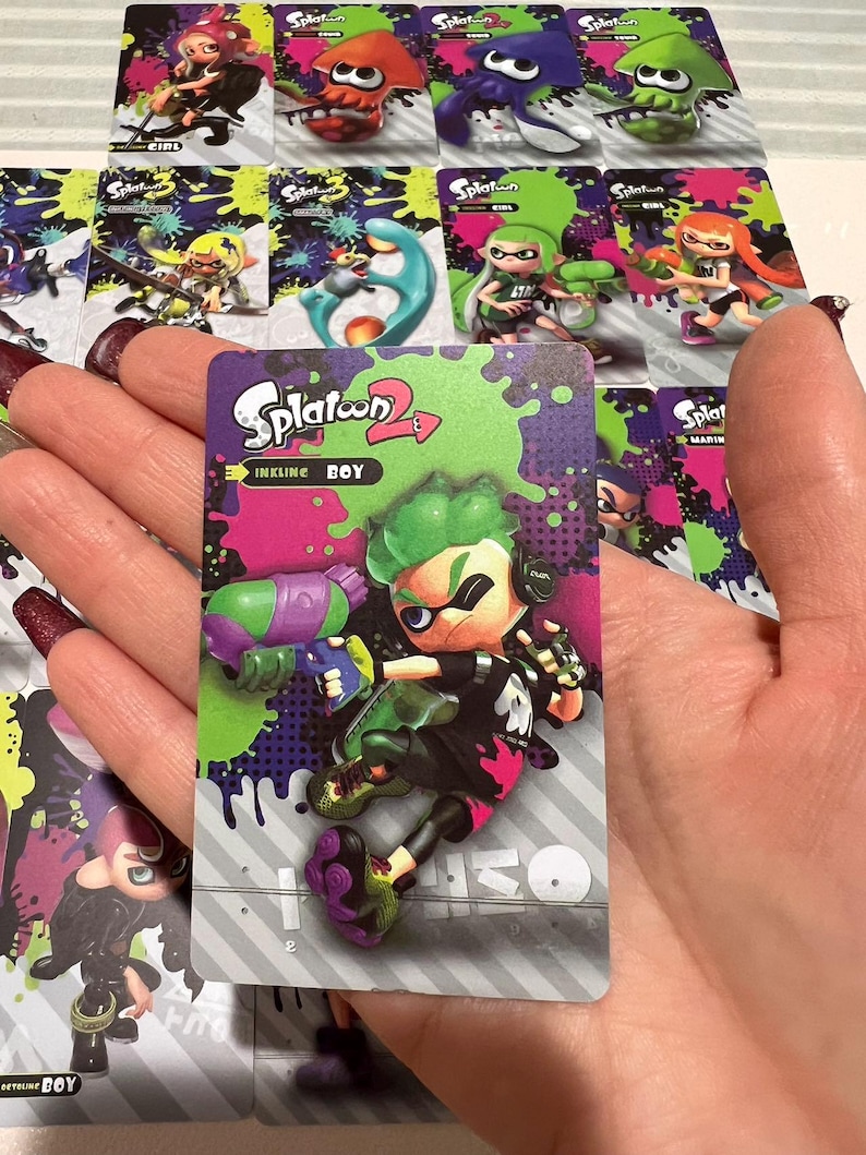 May include: A collection of Splatoon 2 trading cards featuring colorful characters and designs. The central card displays "Inkline Boy" with a green-haired character holding a purple and green weapon. Other cards show various characters and the Splatoon logo.