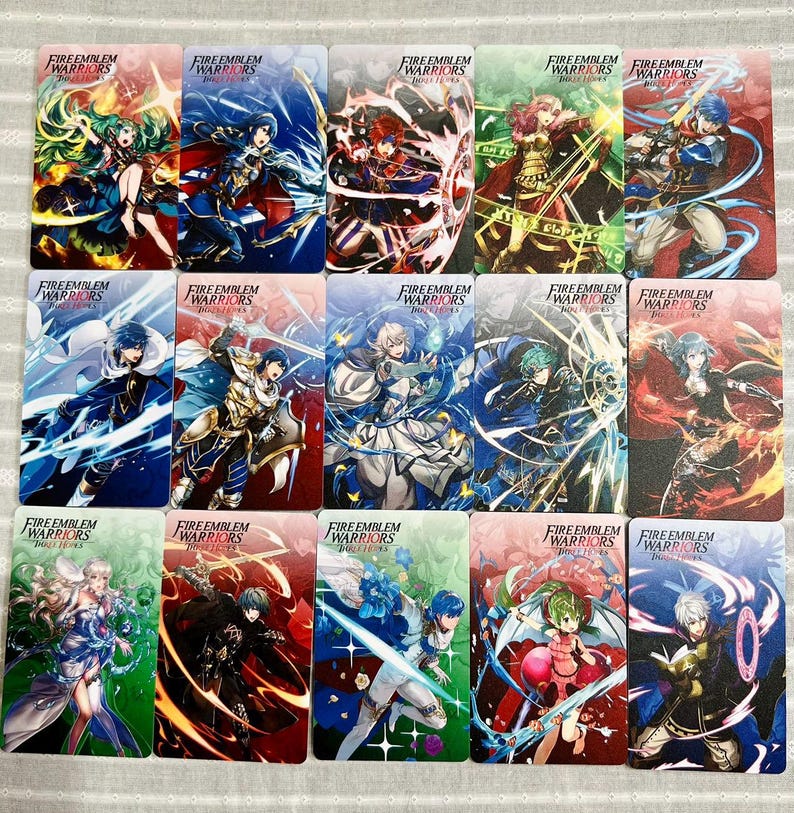 May include: A collection of fifteen rectangular trading cards featuring Fire Emblem Warriors Three Hopes character illustrations. Each card displays a unique anime-style warrior in a dynamic pose with vibrant magical effects, colourful backgrounds, and the Fire Emblem Warriors Three Hopes logo printed at the top.