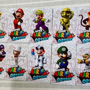 Op de afbeelding: Een set van tien rechthoekige Super Mario Odyssey spelkaarten met diverse personages waaronder Mario, Luigi, Peach, Diddy Kong en Bowser. Elke kaart toont het Super Mario Odyssey logo onderaan tegen een lichte achtergrond met raster.