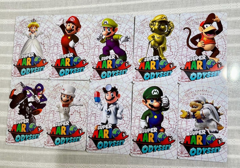 Op de afbeelding: Een set van tien rechthoekige Super Mario Odyssey spelkaarten met diverse personages waaronder Mario, Luigi, Peach, Diddy Kong en Bowser. Elke kaart toont het Super Mario Odyssey logo onderaan tegen een lichte achtergrond met raster.