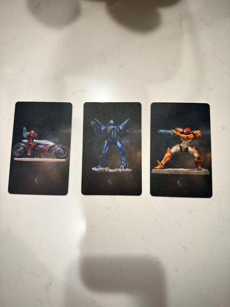 May include: Three trading cards featuring illustrations of characters from a science fiction video game. The cards depict a character on a futuristic motorcycle, a blue robotic figure, and a character in orange and gold armor.