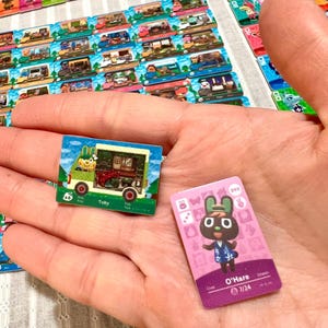 May include: Two rectangular trading cards featuring Animal Crossing characters. One card shows a green camper van with the name Toby, while the other is a pink card featuring a brown rabbit character named O'Hare with the text 7/24 and 390.