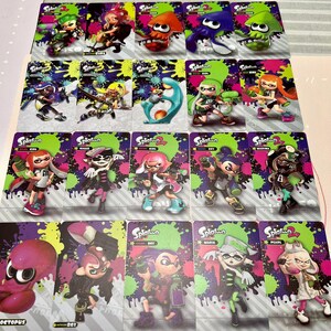 May include: A collection of Splatoon character trading cards. Each card features a different character in vibrant colors, set against a background of green and purple splatters. The cards are arranged in rows and columns.