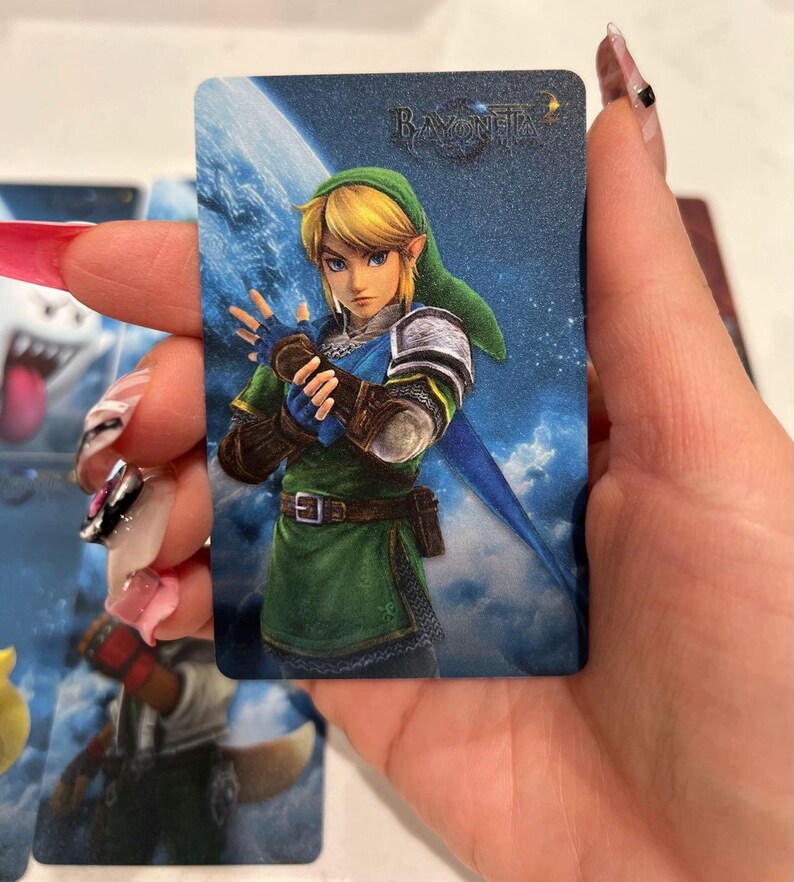 K&ouml;nnte beinhalten: Eine rechteckige Sammelkarte mit einer digitalen Illustration der Figur Link aus der The Legend of Zelda-Reihe, die eine gr&uuml;ne Tunika und M&uuml;tze tr&auml;gt, mit dem Bayonetta-Logo in der oberen rechten Ecke vor einem blauen Weltraumhintergrund.