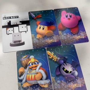 Op de afbeelding: Vijf rechthoekige verzamelkaarten met videogamepersonages. E&eacute;n kaart toont het witte Box Boy-personage met de tekst BOX BOY!. De andere vier kaarten bevatten kleurrijke illustraties van Kirby, Waddle Dee, King Dedede en Meta Knight.