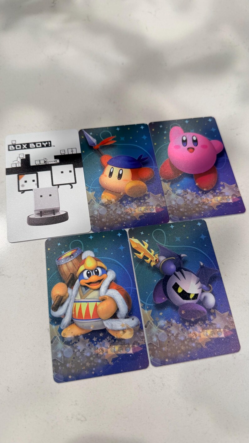 Op de afbeelding: Vijf rechthoekige verzamelkaarten met videogamepersonages. E&eacute;n kaart toont het witte Box Boy-personage met de tekst BOX BOY!. De andere vier kaarten bevatten kleurrijke illustraties van Kirby, Waddle Dee, King Dedede en Meta Knight.