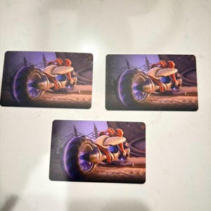 May include: Three rectangular cards featuring a futuristic motorcycle design. The motorcycle has a large front wheel with a purple glow, a white and beige body, and a red-orange rider. The background is a dark, industrial scene.