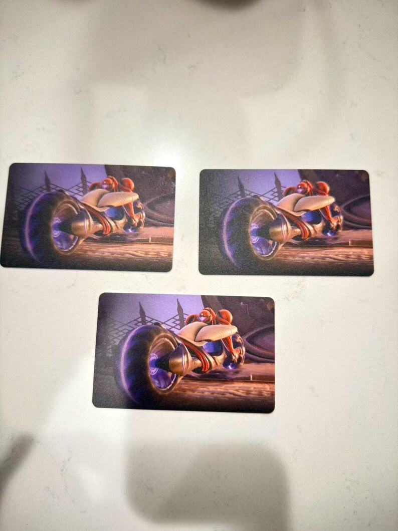 May include: Three rectangular cards featuring a futuristic motorcycle design. The motorcycle has a large front wheel with a purple glow, a white and beige body, and a red-orange rider. The background is a dark, industrial scene.