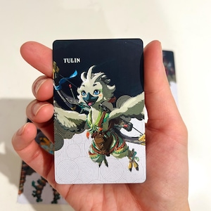 May include: A rectangular trading card featuring a stylized illustration of a white, bird-like creature with blue eyes, green accents, and a bow. The card has a dark blue top section with the text TULIN printed in white and a white bottom section.