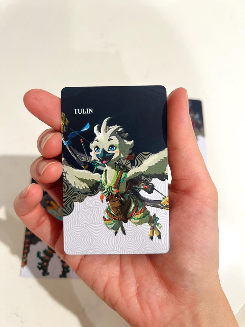 May include: A rectangular trading card featuring a stylized illustration of a white, bird-like creature with blue eyes, green accents, and a bow. The card has a dark blue top section with the text TULIN printed in white and a white bottom section.