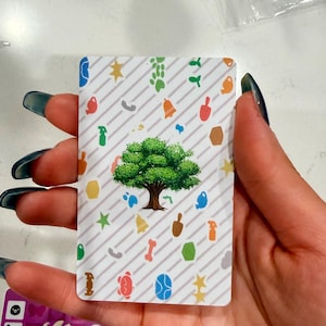 May include: A rectangular trading card featuring a central green tree illustration surrounded by a pattern of small, colourful icons including stars, bells, spray bottles, and paw prints against a white background with diagonal grey stripes.